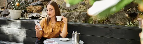 В уютном кафе молодая женщина потягивает кофе, читая сообщения на телефоне, принимая свой образ жизни. — стоковое фото