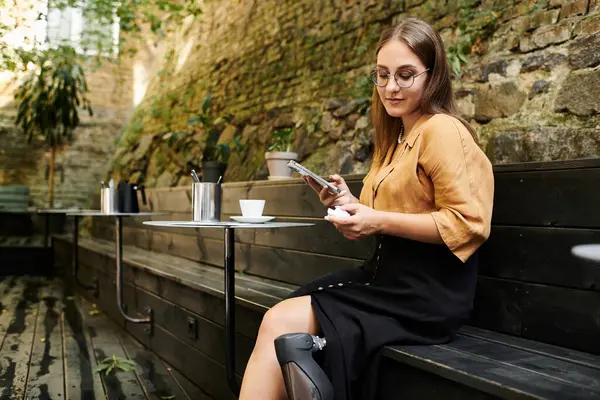 A young woman relaxes in a cozy cafe, engaging with her smartphone while showcasing her prosthetic leg. — Stock Photo