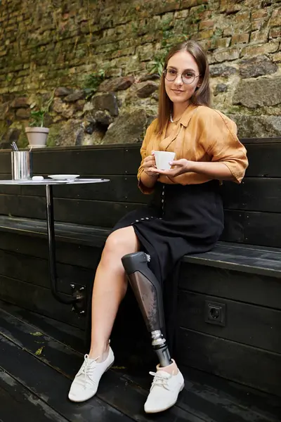A young woman sits in a cafe, sipping coffee and confidently showcasing her prosthetic leg with style. — Stock Photo