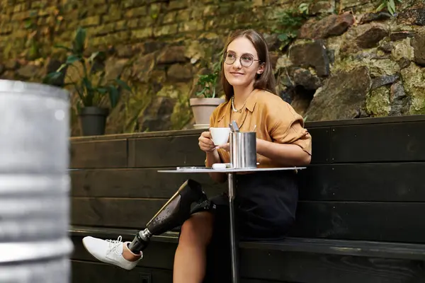 Uma jovem mulher senta-se confortavelmente em um café, saboreando café como ela abraça seu estilo de vida único com uma perna protética. — Fotografia de Stock