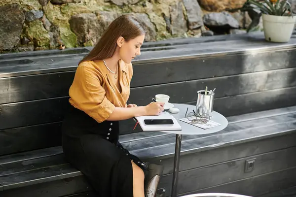 In a serene cafe setting, a young woman with a prosthetic leg writes in her journal while sipping coffee. — Stock Photo