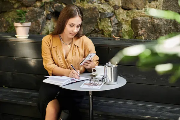 In a cozy cafe, a young woman with a prosthetic leg writes in her notebook while sipping coffee, embracing her daily routine. — Stock Photo