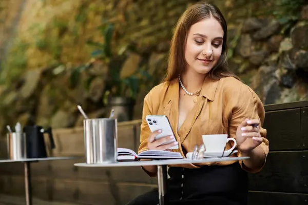 A young woman with a prosthetic leg smiles while sipping tea in a cozy cafe, immersed in her phone and surroundings. — Stock Photo