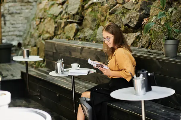 A young woman with a prosthetic leg relaxes in a cafe, sipping coffee and engrossed in a menu, embodying daily life. — Stock Photo