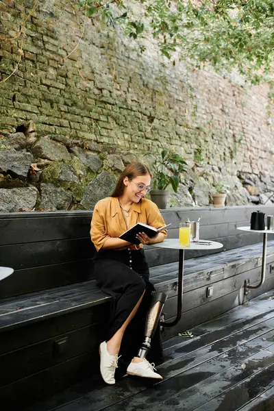 Una joven se sienta cómodamente en un café, leyendo un libro y disfrutando de una bebida refrescante, mostrando su estilo y fuerza únicos. - foto de stock