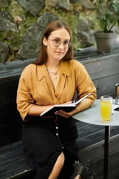 A young woman in casual attire relaxes at a cafe, immersed in her book as she enjoys a refreshing drink. — Stock Photo