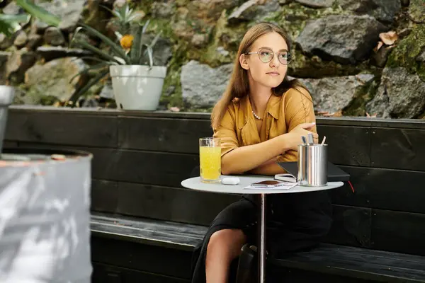 Una joven se relaja en una mesa de café, saboreando su bebida mientras muestra con confianza su pierna protésica, encarnando la resiliencia. - foto de stock
