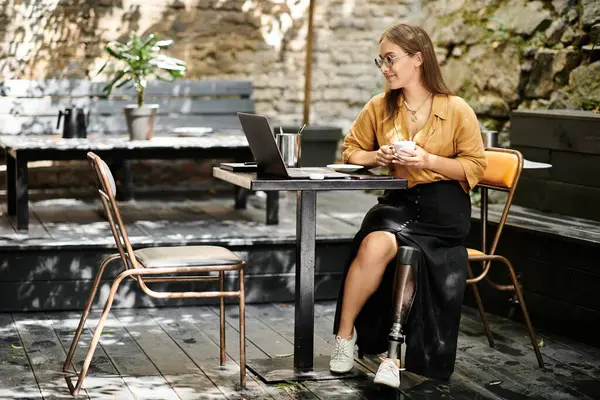 In a cozy cafe setting, a young woman shares a moment with her coffee while working on her laptop, embracing life adventures. — Stock Photo