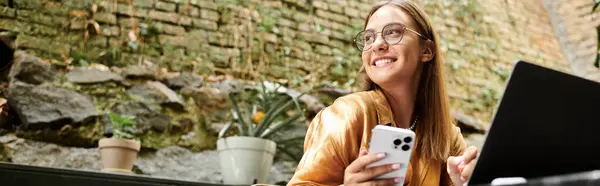 In un accogliente caffè, una giovane donna sorride mentre tiene il telefono, vivendo la vita al massimo. — Foto stock