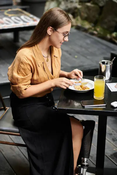 Eine junge Frau mit künstlichen Gliedmaßen sitzt in einem Café und genießt ihr Essen, während sie Zuversicht und Freude ausstrahlt. — Stockfoto