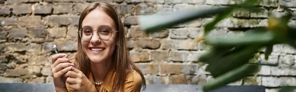 У затишному кафе молода жінка посміхається, тримаючи смартфон — стокове фото