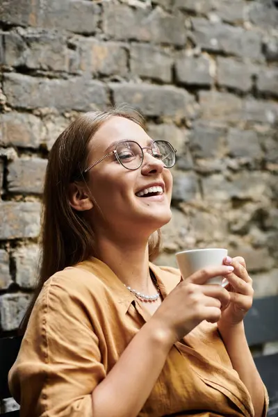 In a welcoming cafe, a young woman smiles while sipping coffee, embracing her daily life. — Stock Photo