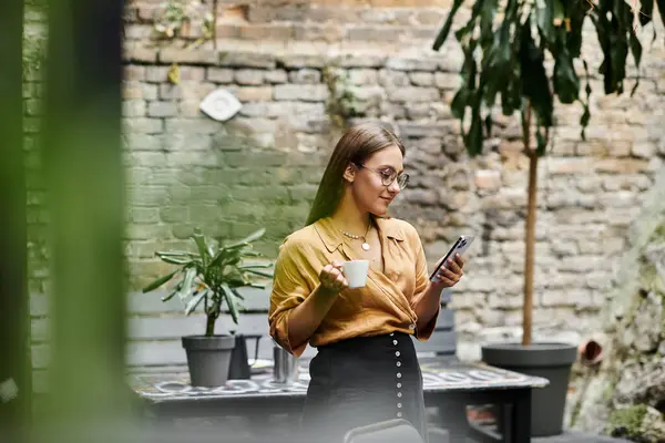 In einem friedlichen Café nippt eine junge Frau am Kaffee, während sie mit ihrem Handy ihre Umgebung umarmt. — Stockfoto