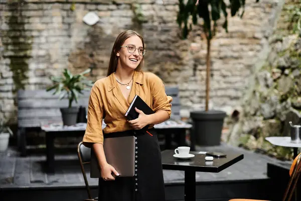 In un affascinante bar, una giovane donna sorride mentre tiene in mano un quaderno, incarnando positività e resilienza.. — Foto stock