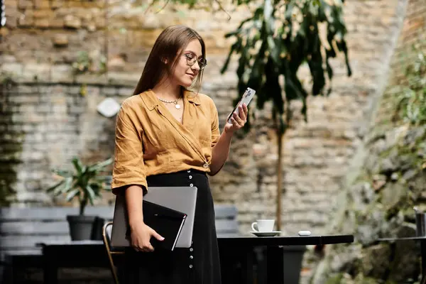 Eine junge Frau in einem gemütlichen Café, lächelnd, während sie ihr Telefon checkt, eine Mischung aus Stil und Komfort. — Stockfoto