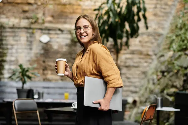 Una giovane donna tiene una tazza di caffè mentre sorride e si prepara a lavorare in un vivace caffè. — Foto stock