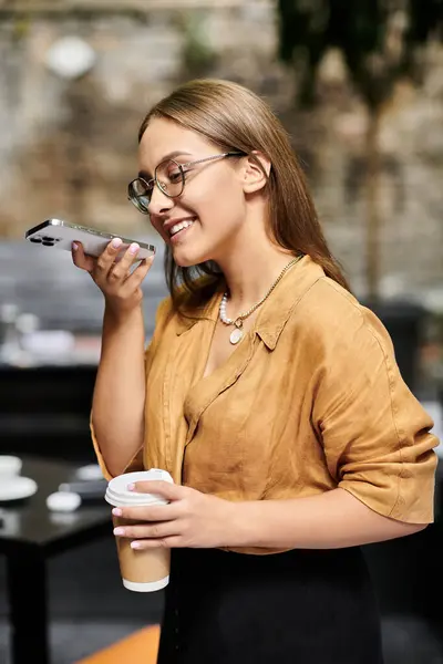 Uma jovem mulher alegremente segura uma xícara de café enquanto conversa em seu telefone em um café. — Fotografia de Stock