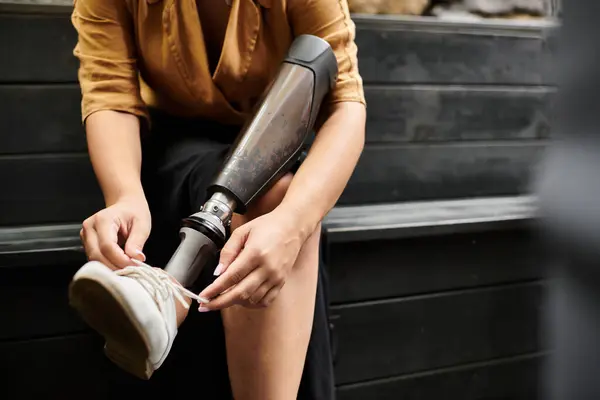 A young woman adjusts her shoe laces in a cozy cafe, embracing a moment of daily life with her artificial limb. — Stock Photo