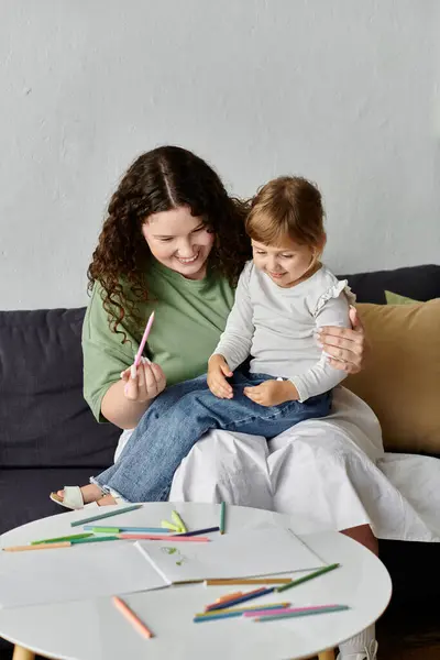 A smiling mother and her young daughter enjoy drawing with colorful crayons on a cozy afternoon. — Stock Photo