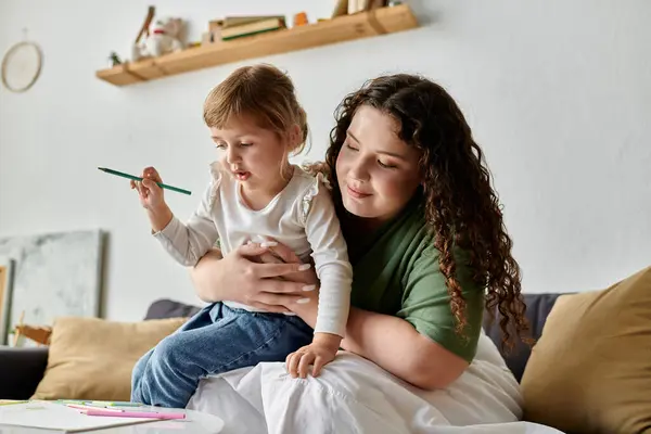 A loving mother cuddles her daughter as they engage in colorful artistic activities on a cozy couch. — Stock Photo