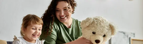 A lively moment of a plus size mother and her daughter enjoying playtime together with a teddy bear. — Stock Photo
