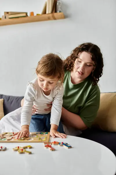 A mother engages with her daughter over a colorful board game while seated comfortably indoors. — Stock Photo