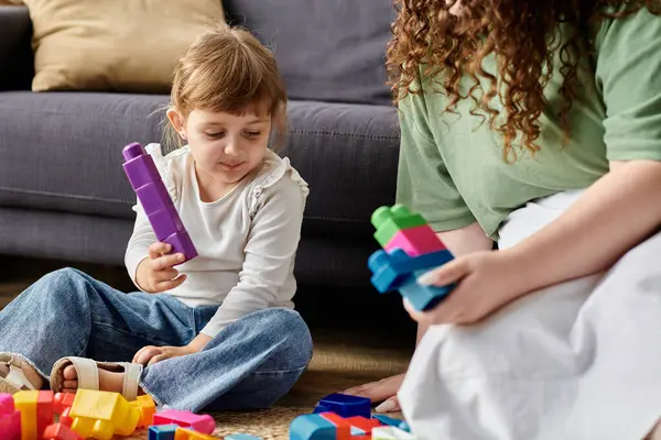A loving mother and her daughter build colorful structures together on the floor. — Stock Photo