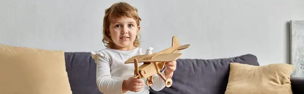 Petite adorable fille assise sur un canapé et jouant avec son avion jouet à la maison. — Photo de stock