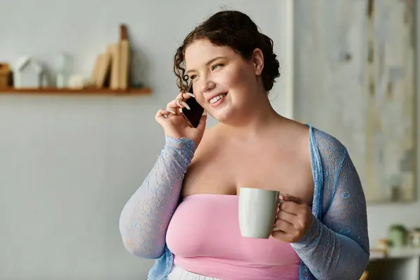 Прекрасная женщина plus size наслаждается случайным разговором, держа в руках горячую чашку кофе и улыбаясь. — стоковое фото