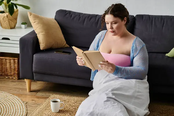 Gut gekleidete Plus-Size-Frau in gemütlicher Homewear mit Buch in der Nähe der Teetasse, zu Hause. — Stockfoto