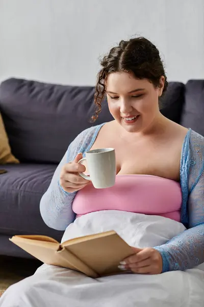 Cheerful plus size woman in cozy homewear holding tea cup in hands, at home. — Stock Photo