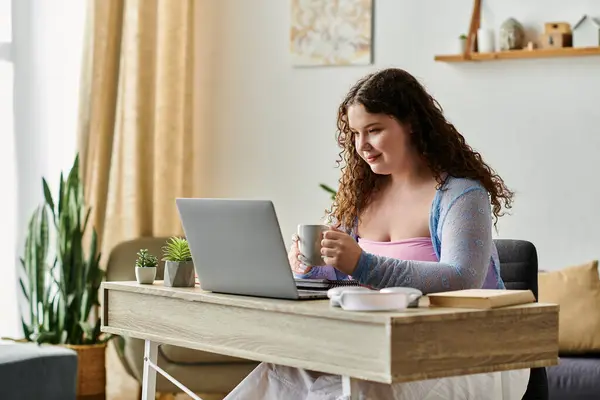 Femme positive de taille plus avec les cheveux bouclés en tenue confortable travaillant à la maison. — Photo de stock