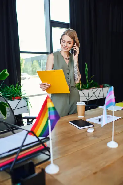 Un empleado alegre realiza una llamada telefónica mientras revisa documentos en un espacio de trabajo vibrante. - foto de stock