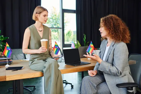 Due colleghi si impegnano in una conversazione vibrante sorseggiando caffè e celebrando l'orgoglio. — Foto stock