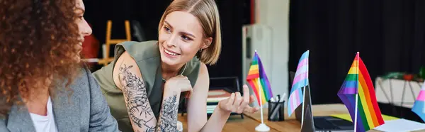 Zwei Kollegen teilen Ideen und lachen in einem lebhaften Büro voller Stolz-Fahnen. — Stockfoto