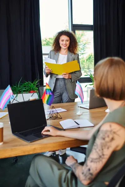 Coworkers discuss inclusive strategies while showcasing pride flags in a vibrant workspace. — Stock Photo