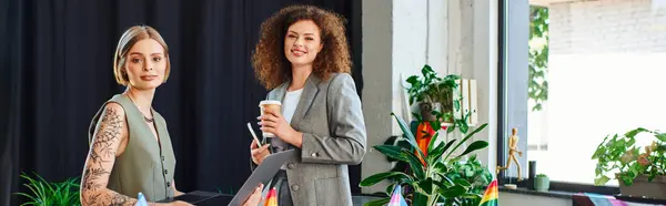 Two coworkers chat animatedly among plants and vibrant flags, highlighting diversity. — Stock Photo