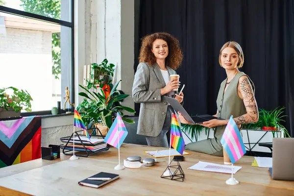 Two colleagues engage warmly in an office setting filled with vibrant decor and pride symbols. — Stock Photo