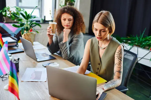 In a lively workspace, two colleagues engage in a focused discussion while working on laptops. — Stock Photo