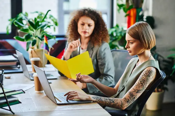 Two coworkers share ideas at a colorful office workspace, celebrating diversity and teamwork. — Stock Photo