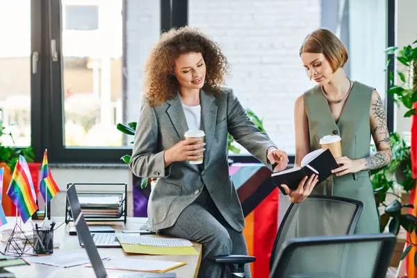 Two colleagues engage in a discussion over a notebook, surrounded by symbols of pride and inclusion. — Stock Photo