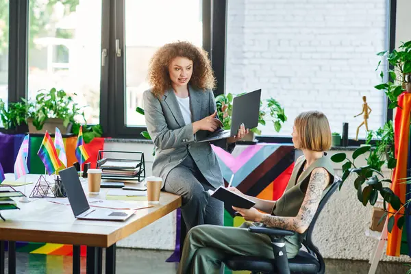 Two coworkers engage in a lively discussion, surrounded by colorful pride flags and plants. — Stock Photo