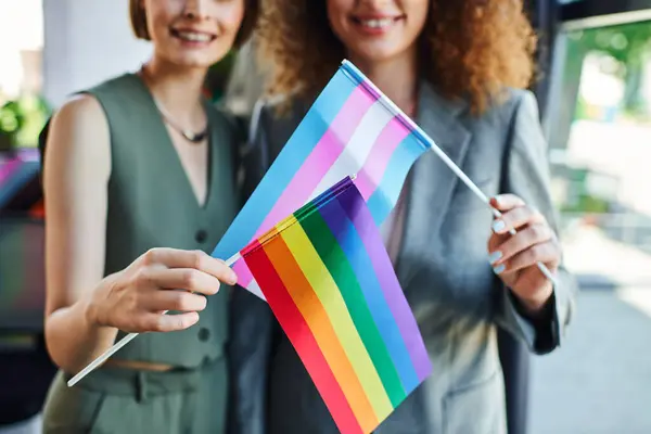Two coworkers joyfully display pride flags, symbolizing inclusivity and support at work. — Stock Photo