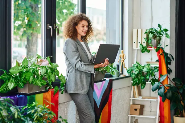 A professional woman engages with her laptop among vibrant plants and colorful pride flags. — Stock Photo