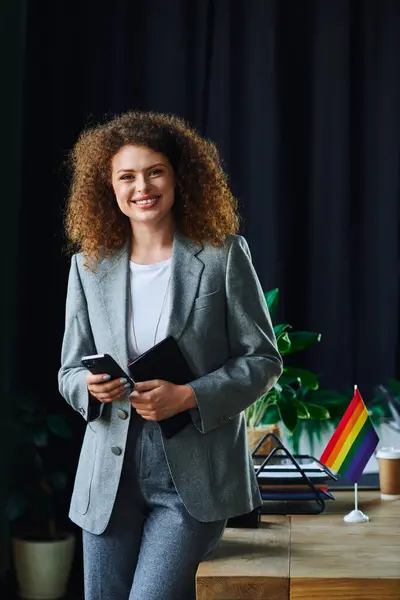 A cheerful coworker holds a smartphone and notebook, embodying support for the LGBTQ community. — Stock Photo