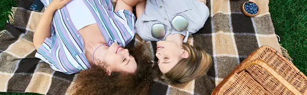 Duas jovens mulheres compartilham momentos alegres enquanto relaxam em um cobertor de piquenique ao ar livre. — Fotografia de Stock