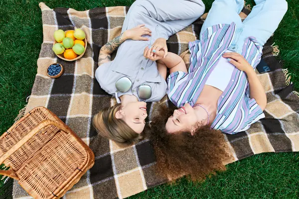 Two friends relax on a blanket, sharing laughter and moments in the sunshine with fruits nearby. — Stock Photo