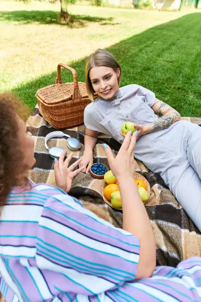 Dois amigos relaxam em um cobertor, desfrutando de frutas frescas e companhia uns dos outros sob o sol. — Fotografia de Stock