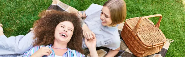 Dos mujeres jóvenes disfrutan de la risa y la amistad mientras yacen en una manta de picnic en la hierba. - foto de stock