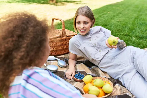 Two friends relax on a blanket, savoring fresh fruits and enjoying each others company in the sun. — Stock Photo